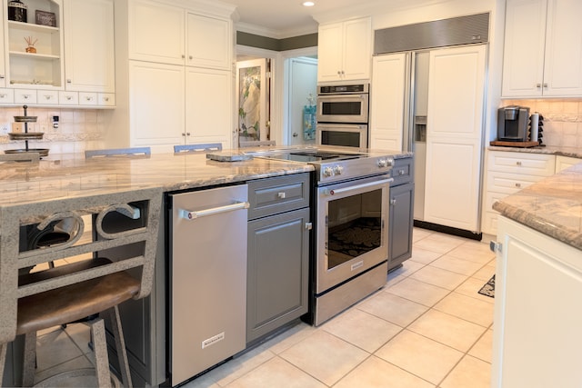 kitchen featuring ornamental molding, light stone counters, white cabinetry, appliances with stainless steel finishes, and light tile patterned floors