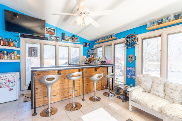 bar featuring tile patterned floors, bar, ceiling fan, and vaulted ceiling