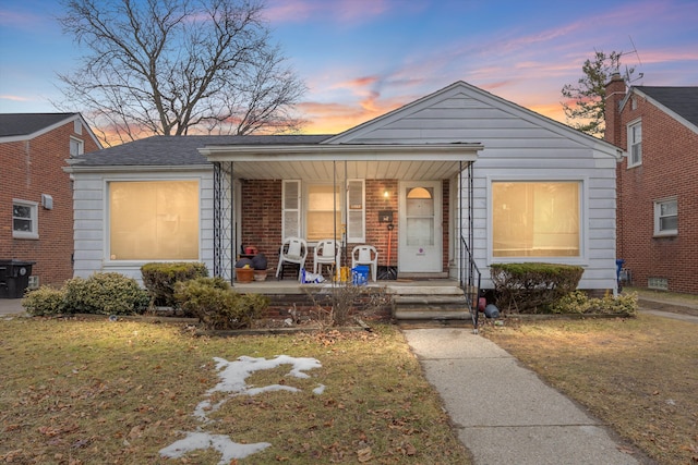 bungalow-style home with brick siding, covered porch, and a lawn