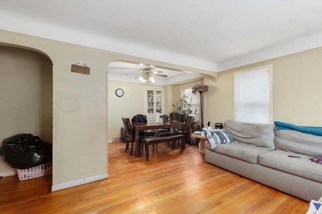 living room featuring arched walkways, light wood-style flooring, a ceiling fan, and baseboards