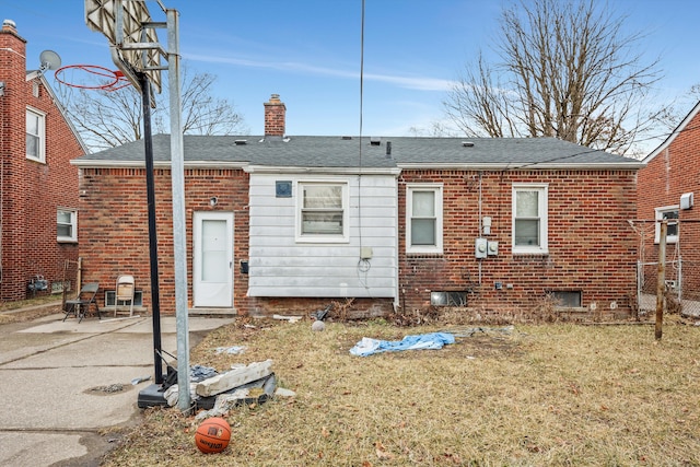 rear view of house featuring brick siding, roof with shingles, a chimney, a yard, and a patio area