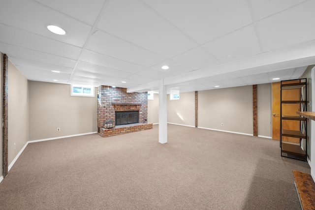 below grade area with a paneled ceiling, baseboards, a brick fireplace, and carpet flooring