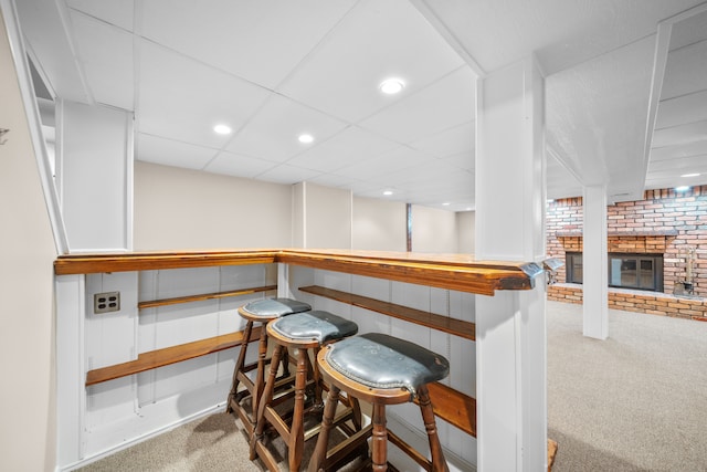 bar featuring a drop ceiling, a fireplace, a bar, and carpet floors