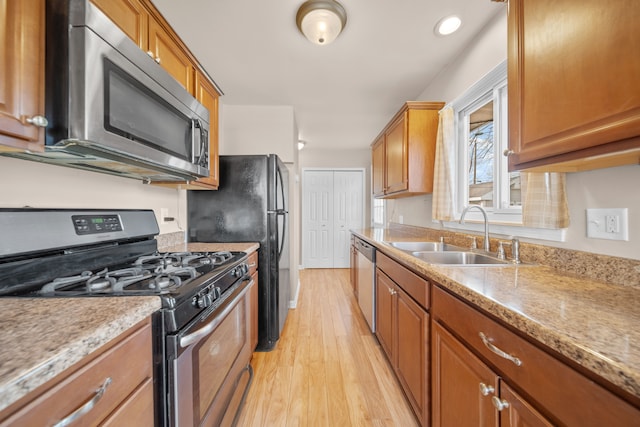 kitchen featuring light wood finished floors, recessed lighting, appliances with stainless steel finishes, brown cabinetry, and a sink