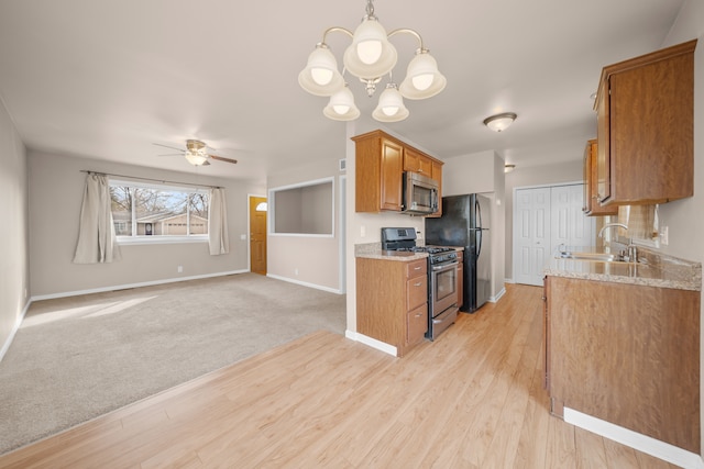 kitchen featuring brown cabinetry, a sink, stainless steel appliances, light carpet, and ceiling fan with notable chandelier