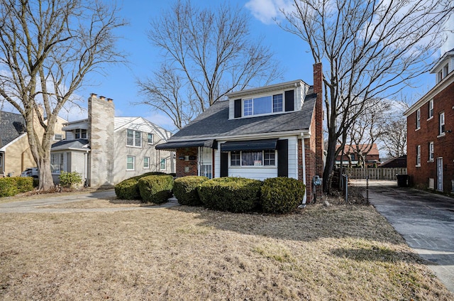 view of front facade with brick siding, a chimney, and a shingled roof