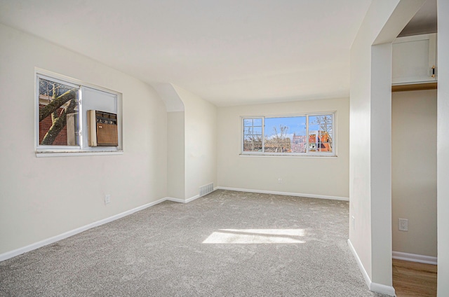 empty room with arched walkways, baseboards, visible vents, and light carpet