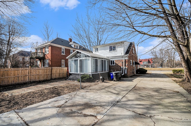 rear view of house with fence, brick siding, a chimney, and a sunroom