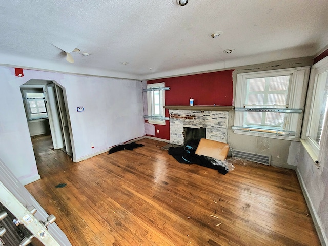 20048 Fleming St, Detroit, MI 48234 - unfurnished living room with a textured ceiling, visible vents, a fireplace, arched walkways, and wood-type flooring