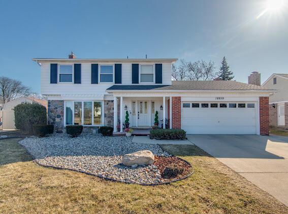 traditional-style home featuring driveway, an attached garage, covered porch, a front lawn, and brick siding