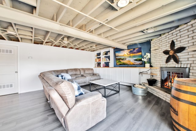 living room with visible vents, a brick fireplace, and wood finished floors