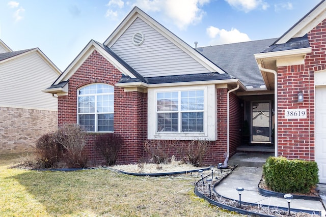 view of front of house featuring brick siding, a shingled roof, and a front yard