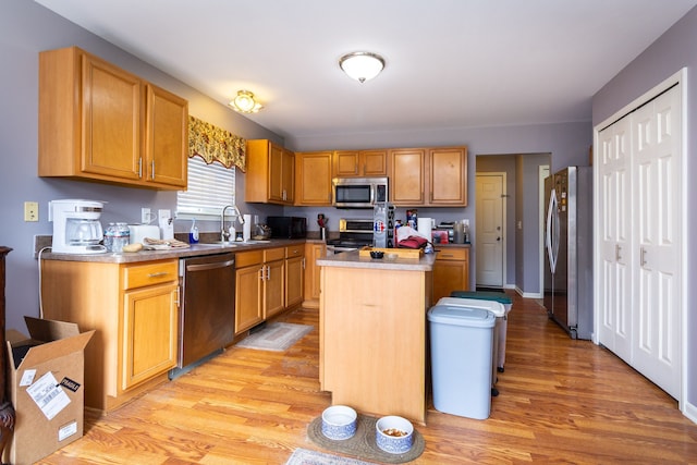 kitchen with light wood-type flooring, a sink, a center island, appliances with stainless steel finishes, and light countertops