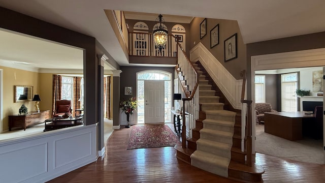 entrance foyer featuring a notable chandelier, stairway, dark wood-type flooring, and crown molding