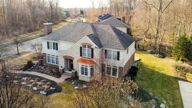 view of front facade featuring a shingled roof, a front lawn, and a chimney