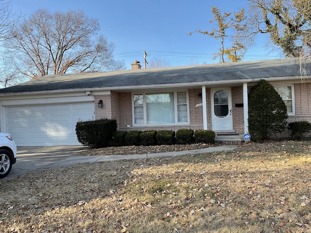 single story home featuring driveway, an attached garage, a shingled roof, brick siding, and a chimney