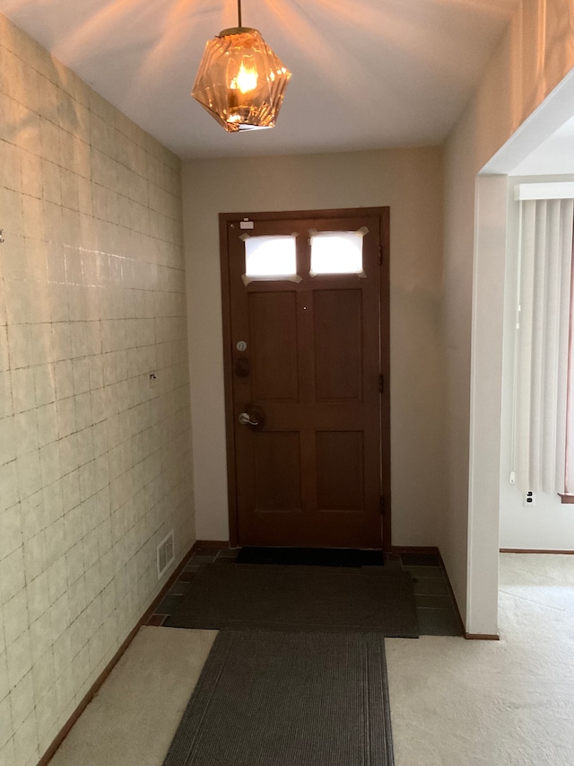 doorway with baseboards, visible vents, tile walls, and carpet