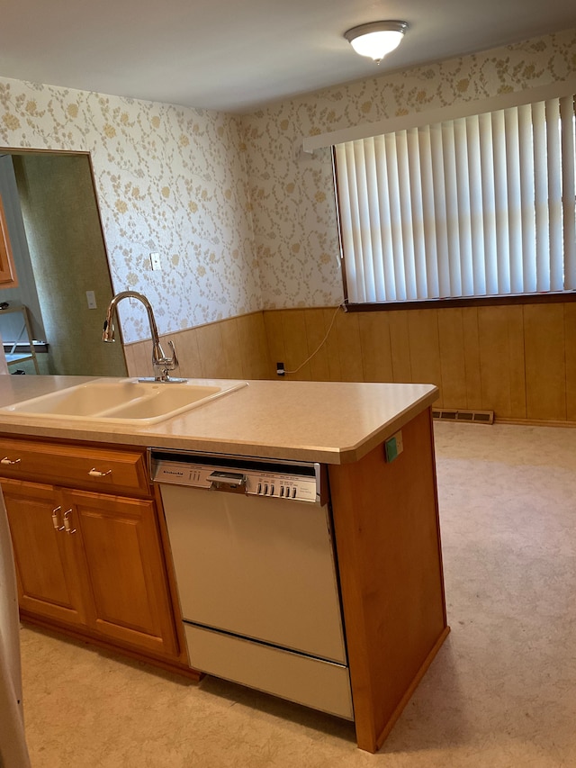 kitchen with dishwashing machine, brown cabinetry, visible vents, wallpapered walls, and a sink