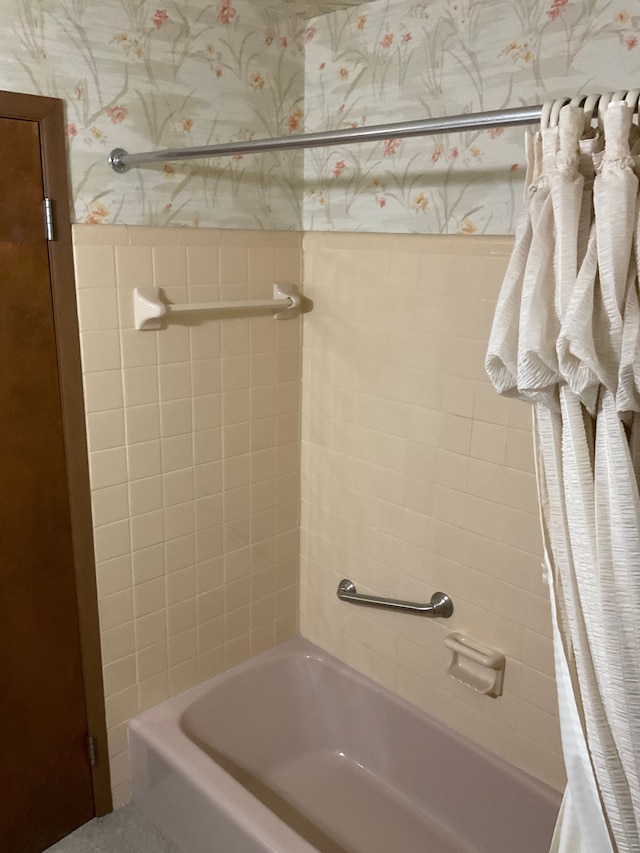 bathroom with wallpapered walls, shower / bathtub combination with curtain, and wainscoting