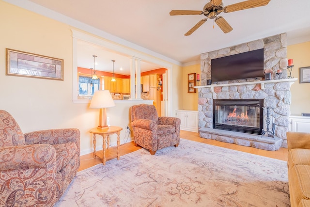 living room featuring a stone fireplace, ceiling fan, wood finished floors, and ornamental molding