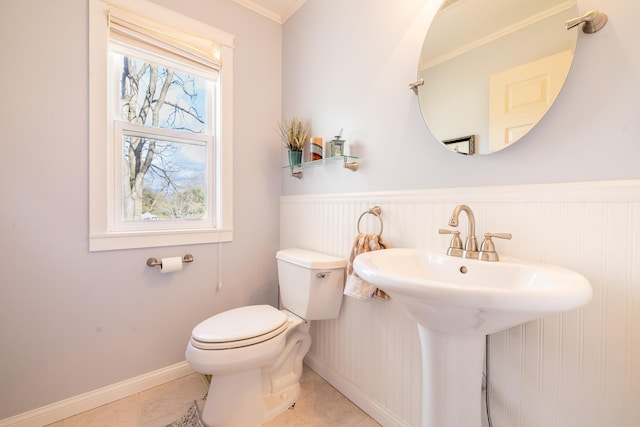 half bath featuring tile patterned floors, a wainscoted wall, baseboards, and toilet