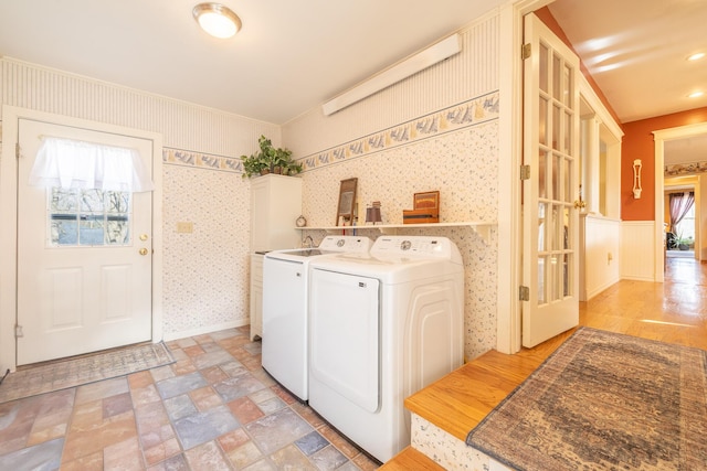 laundry area featuring washer and clothes dryer, stone finish floor, cabinet space, wainscoting, and wallpapered walls