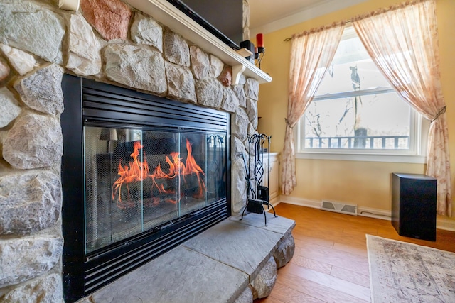 interior details featuring visible vents, baseboards, a stone fireplace, and wood finished floors