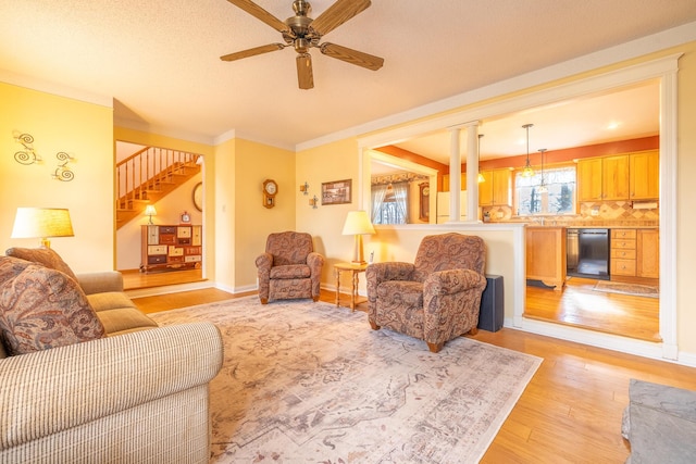 living room featuring crown molding, baseboards, stairway, light wood-type flooring, and a ceiling fan