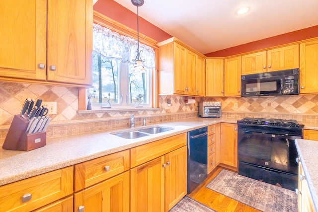 kitchen with black appliances, a sink, light wood finished floors, decorative backsplash, and hanging light fixtures