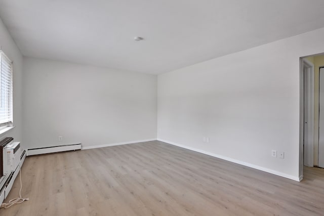 spare room with a baseboard heating unit, light wood-type flooring, and baseboards