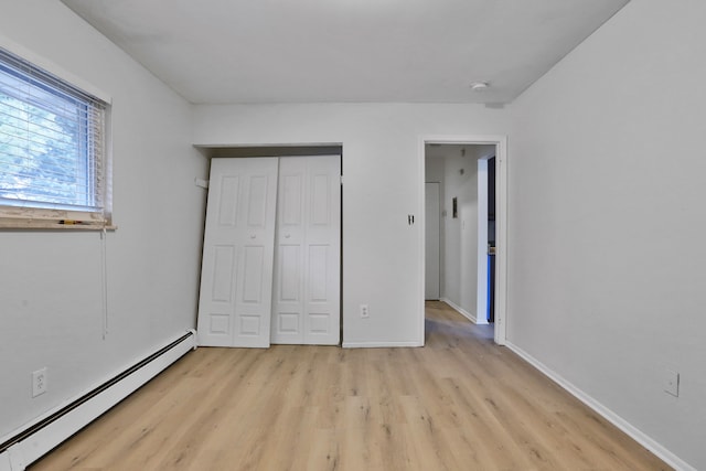 unfurnished bedroom featuring a baseboard heating unit, light wood-style flooring, baseboards, and a closet