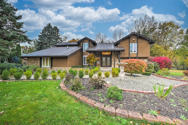 tri-level home featuring a front yard, french doors, stone siding, and a shingled roof