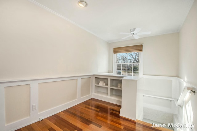 spare room featuring a ceiling fan, wood finished floors, a wainscoted wall, and ornamental molding