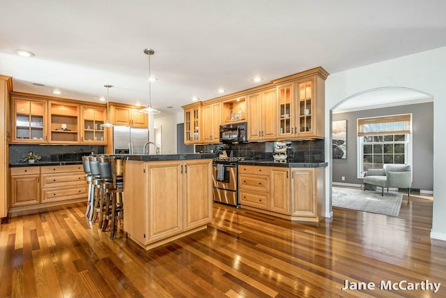 kitchen with arched walkways, stainless steel appliances, dark countertops, and tasteful backsplash