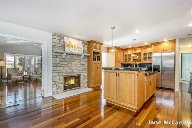 kitchen with visible vents, dark countertops, a kitchen island, stainless steel fridge, and a fireplace