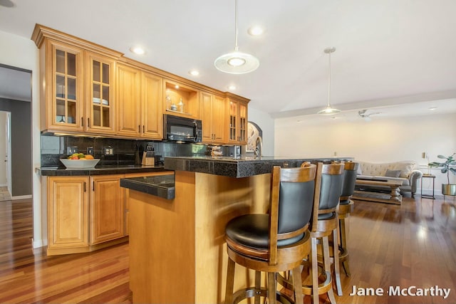 kitchen with wood finished floors, tasteful backsplash, a breakfast bar area, and black microwave