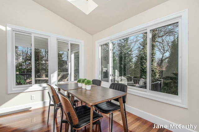 dining room with baseboards, vaulted ceiling with skylight, a healthy amount of sunlight, and wood finished floors