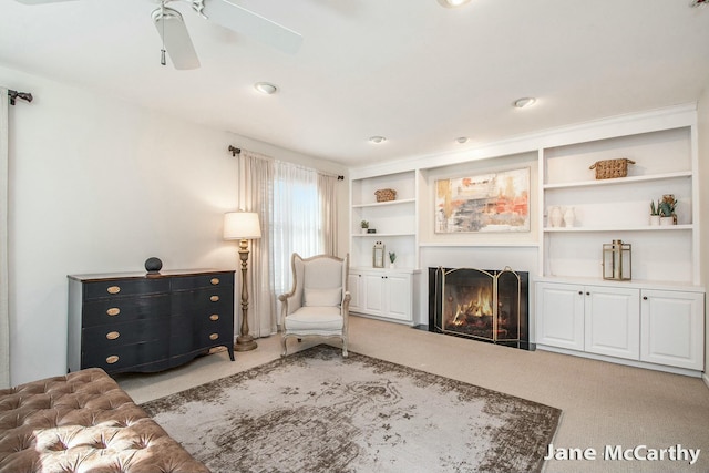 sitting room featuring carpet, a warm lit fireplace, and ceiling fan