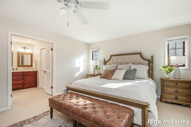 bedroom featuring light colored carpet, ensuite bath, baseboards, and a sink