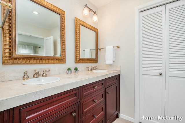 full bathroom with double vanity, a closet, baseboards, and a sink