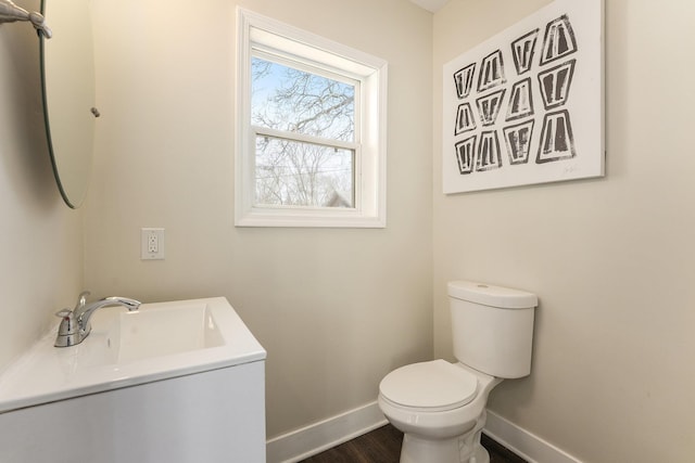 half bathroom with toilet, vanity, baseboards, and wood finished floors