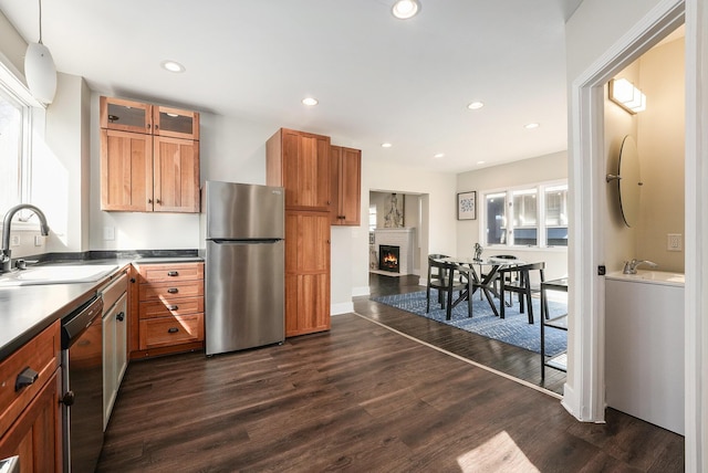 kitchen with a sink, a lit fireplace, recessed lighting, appliances with stainless steel finishes, and dark wood-style flooring