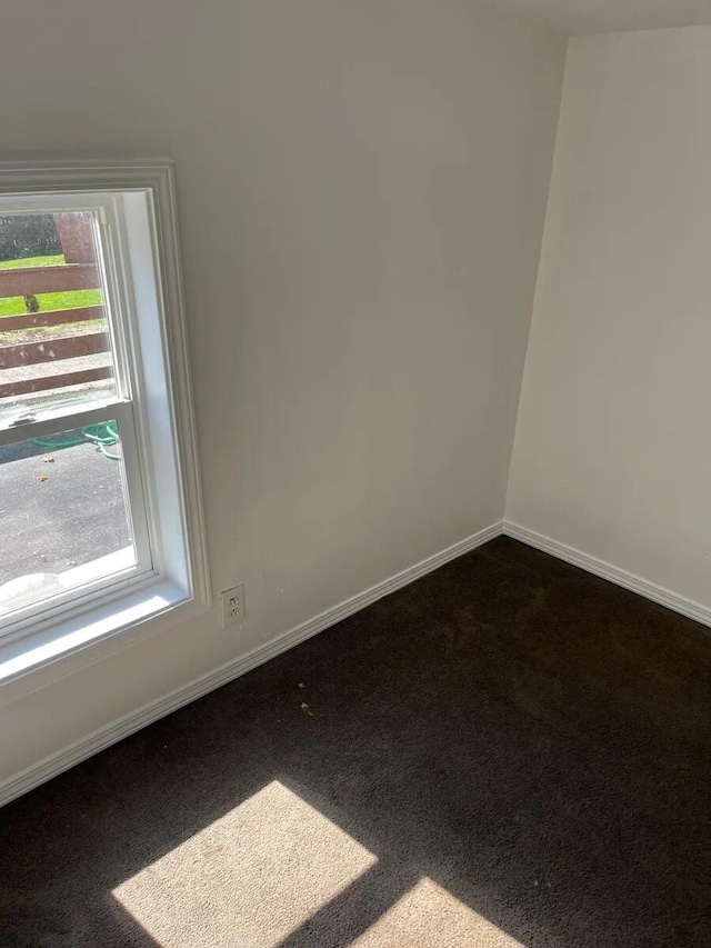 unfurnished room featuring baseboards, a healthy amount of sunlight, and dark carpet