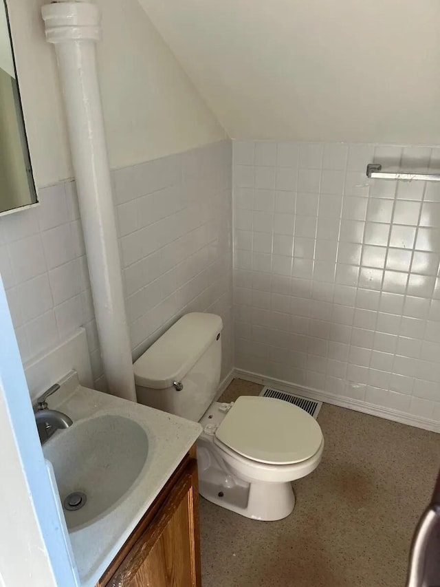 half bath featuring vanity, visible vents, speckled floor, tile walls, and toilet