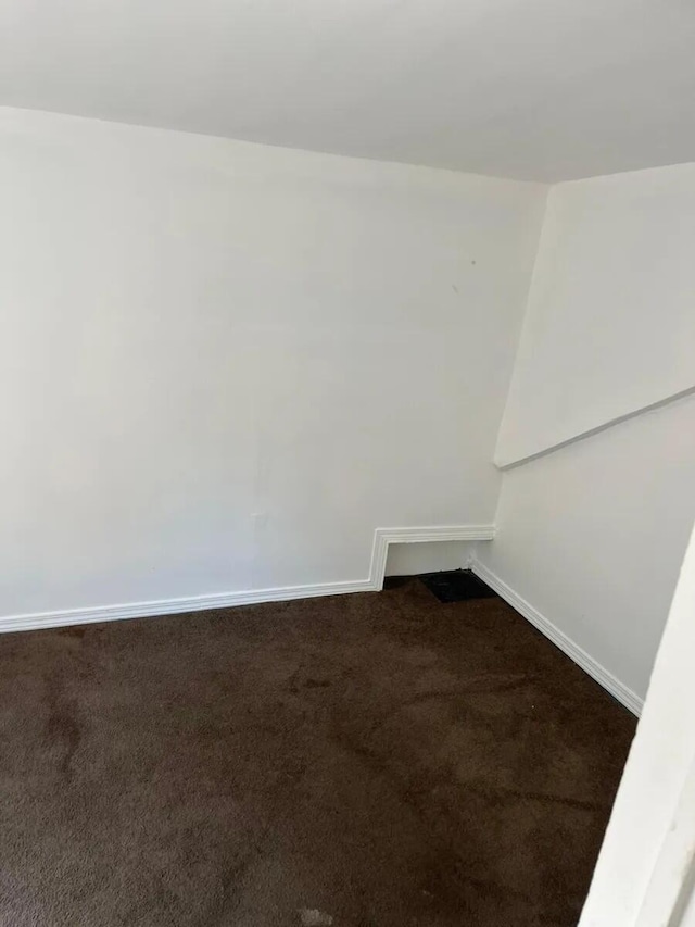 spare room with baseboards and dark colored carpet