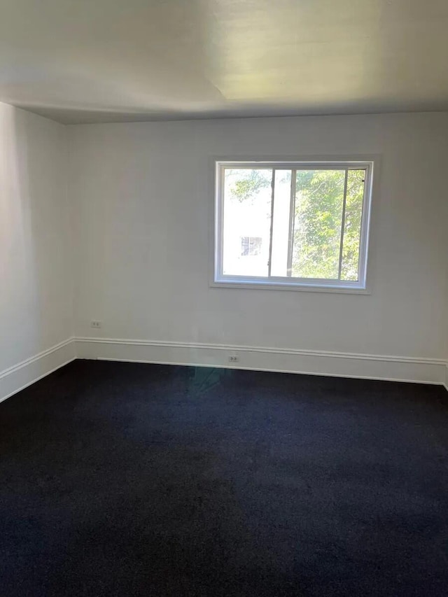 spare room featuring dark carpet and baseboards