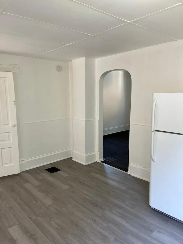 unfurnished room featuring arched walkways, baseboards, and wood finished floors