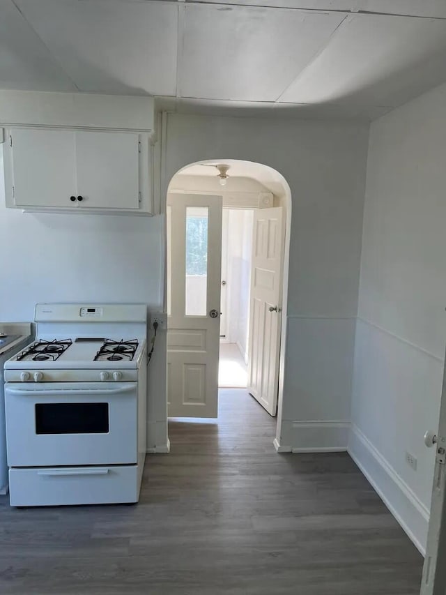 kitchen featuring baseboards, white range with gas stovetop, wood finished floors, arched walkways, and white cabinetry