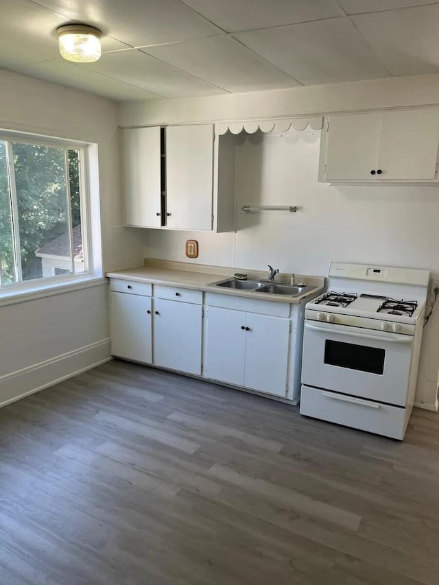 kitchen featuring a sink, wood finished floors, white cabinetry, light countertops, and white gas range