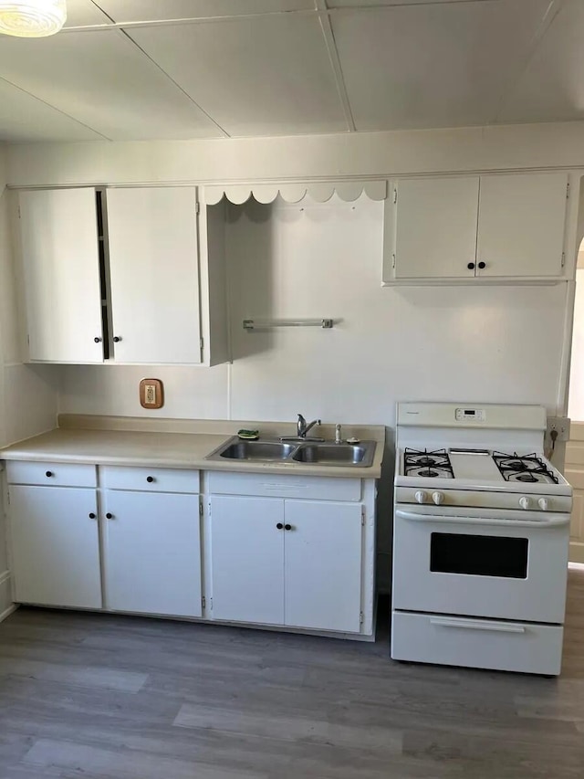 kitchen featuring light countertops, white gas range oven, wood finished floors, white cabinets, and a sink